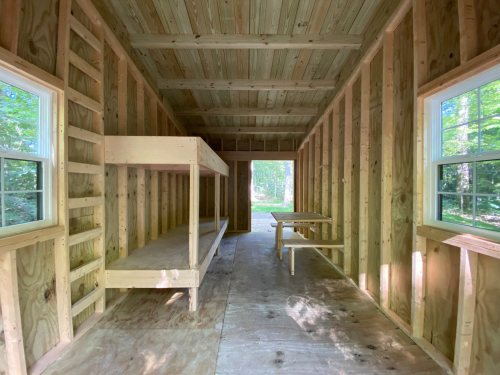 Interior of a wooden cabin with two bunk beds, a table, and large windows letting in natural light.