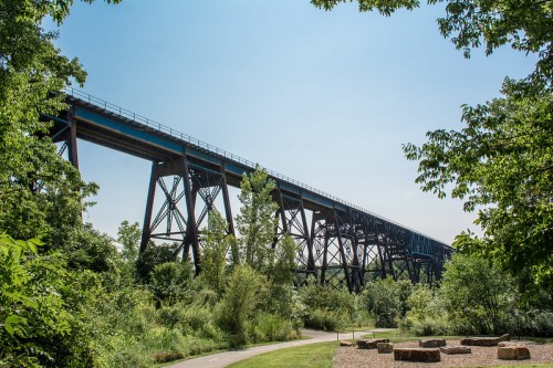 A tall railway bridge spans over lush greenery under a clear blue sky, with a path leading through the park below.