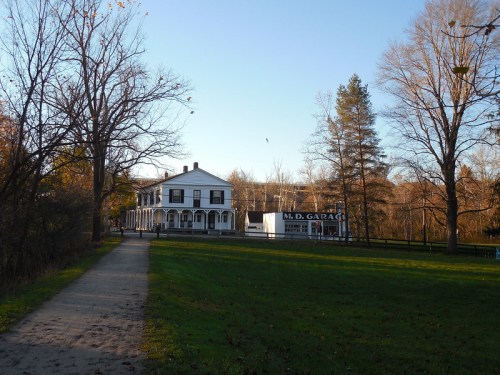 A scenic view of a white building with a porch, surrounded by trees and a grassy path leading towards it.