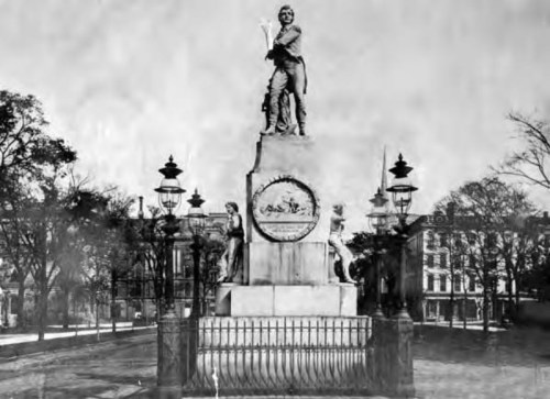 A historic monument featuring a statue atop a pedestal, surrounded by decorative lamps and trees.