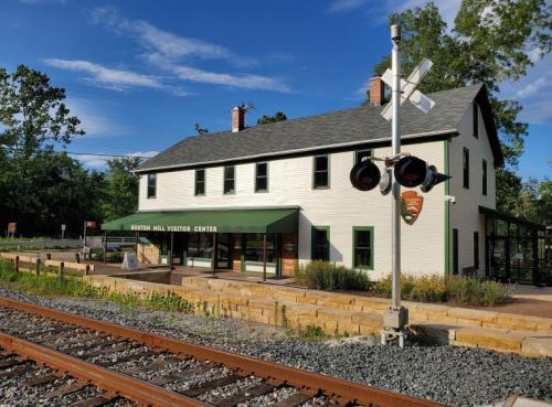 Historic visitor center building with green awning, surrounded by greenery and railway tracks in the foreground.