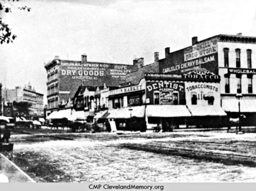 Historic street scene featuring storefronts with signs for dry goods, tobacco, and a dentist, in a snowy setting.