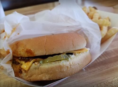 A cheeseburger with pickles in a wrapper, accompanied by crinkle-cut fries on a wooden table.