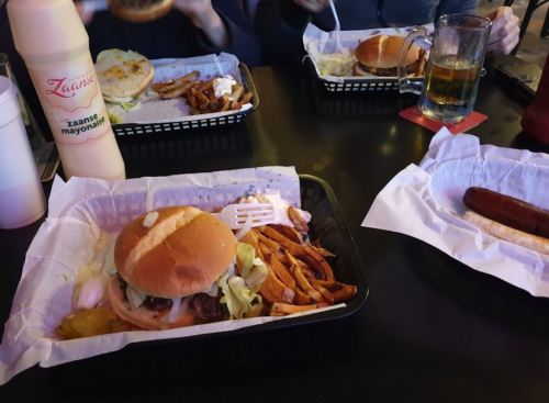 A table with burgers, fries, and drinks in baskets, with a bottle of mayonnaise in the foreground.