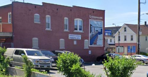 A brick building with a sign for "Landmark Restaurant" and parked cars in front, under a clear blue sky.