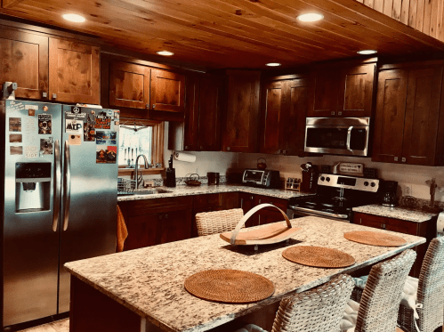 A cozy kitchen with wooden cabinets, granite countertops, stainless steel appliances, and a large island with woven placemats.