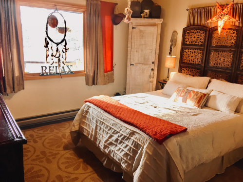 Cozy bedroom with a white bedspread, orange accents, and decorative elements, featuring a window and a dreamcatcher.