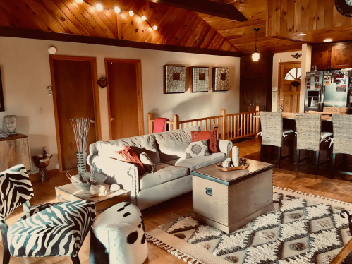 Cozy living room with a sofa, patterned chairs, wooden accents, and a dining area in a warm, inviting space.
