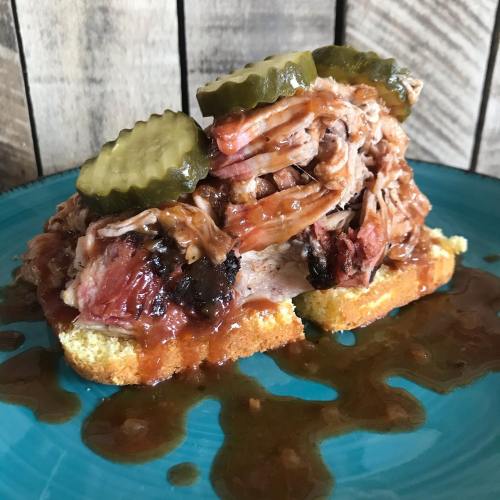 A sandwich with pulled pork, pickles, and barbecue sauce on a slice of bread, served on a blue plate.