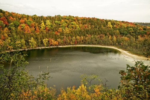 A serene lake surrounded by vibrant autumn foliage in shades of orange, yellow, and green.