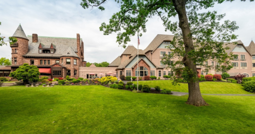 A picturesque view of a historic mansion surrounded by lush green lawns and colorful gardens.