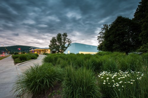 A modern building surrounded by lush greenery and flowers, under a dramatic cloudy sky.
