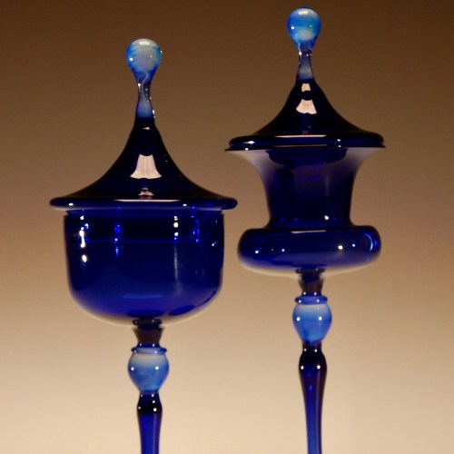 Two elegant blue glass containers with lids, featuring smooth curves and a glossy finish, set against a soft background.