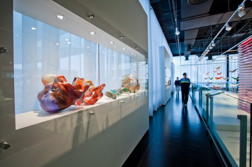 A modern gallery showcasing colorful glass sculptures under soft lighting, with a visitor walking through.