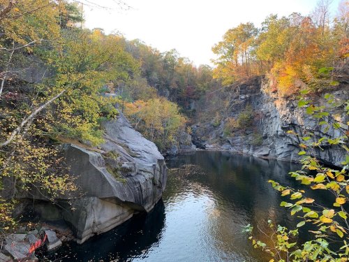 A serene river flows between rocky cliffs, surrounded by vibrant autumn foliage and a clear sky.