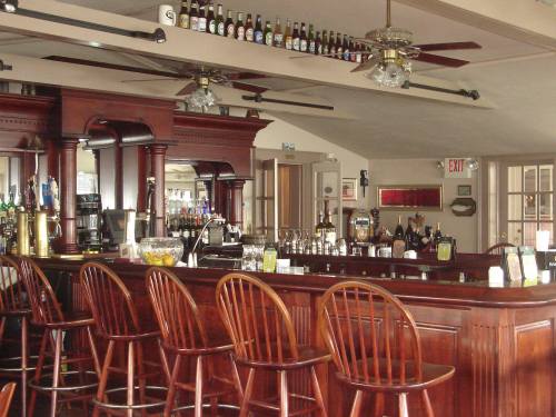 A wooden bar with high stools, shelves of bottles above, and a cozy, inviting atmosphere.