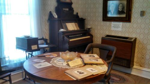 A vintage room featuring a wooden table with books, an organ, and historical photographs on the wall.
