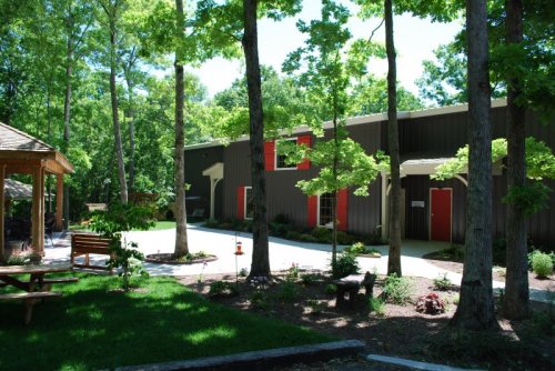 A modern building surrounded by trees and greenery, featuring red doors and a nearby gazebo with seating.