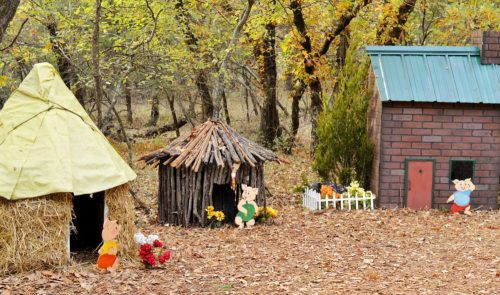 Three whimsical houses made of straw, sticks, and bricks, surrounded by autumn leaves and trees.