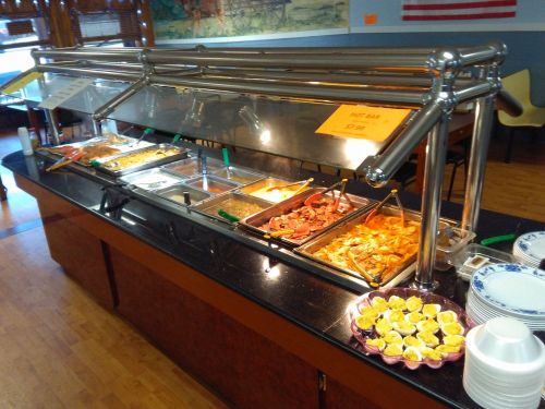 A buffet with various dishes in metal trays, including meats and sides, and a plate of lemon slices in front.