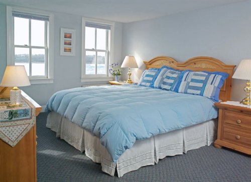 Cozy bedroom with a large blue comforter, two lamps, and windows overlooking a scenic view.
