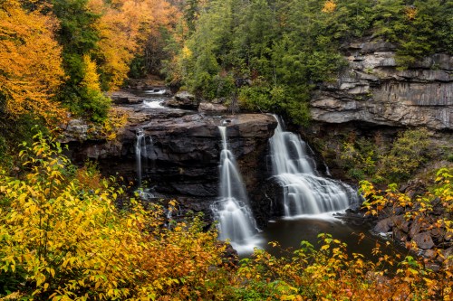 A serene waterfall cascades over rocky cliffs, surrounded by vibrant autumn foliage in a tranquil forest setting.