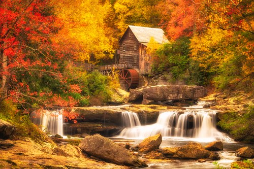 A rustic wooden mill beside a waterfall, surrounded by vibrant autumn foliage and rocky terrain.