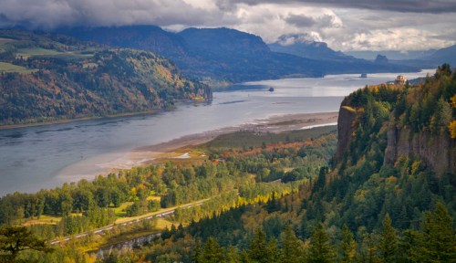 A scenic view of a river winding through lush green forests and mountains under a cloudy sky.