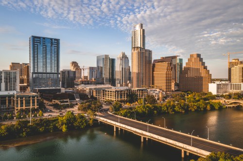 Aerial view of Austin's skyline with modern buildings and a river, under a partly cloudy sky.