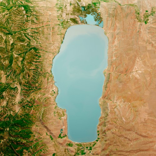 Aerial view of a large, elongated lake surrounded by varied terrain, with green areas and dry land visible nearby.