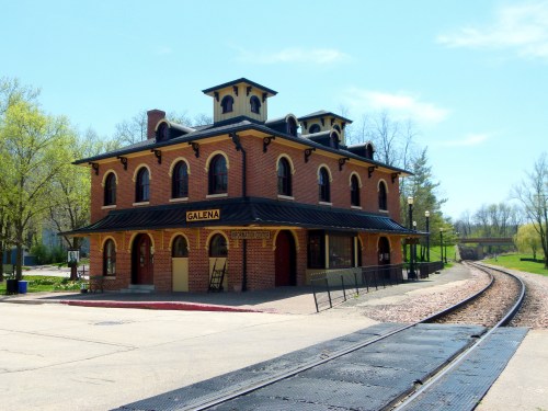 Historic brick train station in Galena, with a clear blue sky and railway tracks in the foreground.