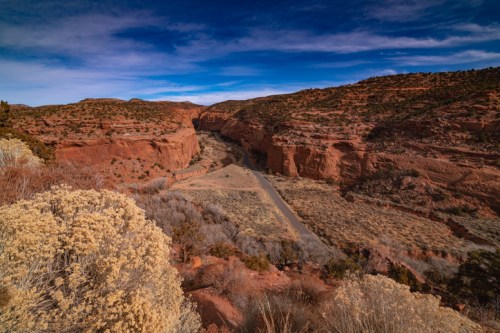 A scenic view of a winding road through red rock canyons under a blue sky with scattered clouds.
