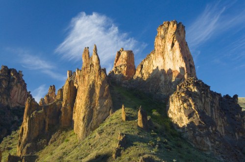 Majestic rock formations rise against a blue sky with wispy clouds, showcasing rugged textures and vibrant colors.