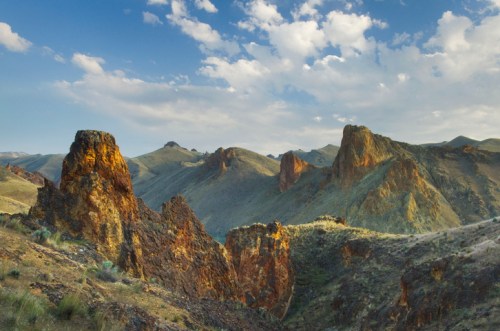 A scenic view of rugged mountains and rocky formations under a blue sky with scattered clouds.