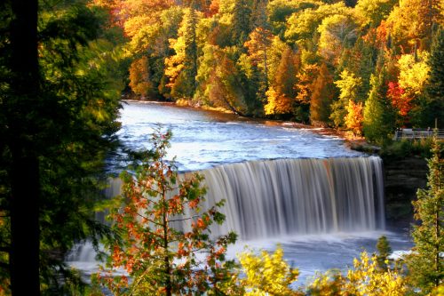 A serene waterfall surrounded by vibrant autumn foliage in a lush forest.