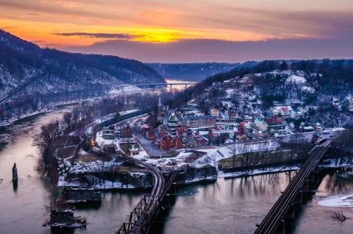A scenic view of a river town at sunset, with snow-covered hills and bridges in the foreground.
