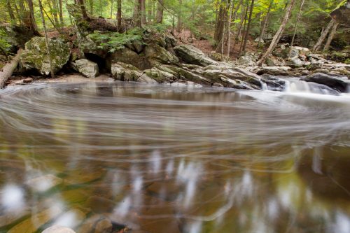 A serene river scene with swirling water, surrounded by lush green trees and rocky banks.