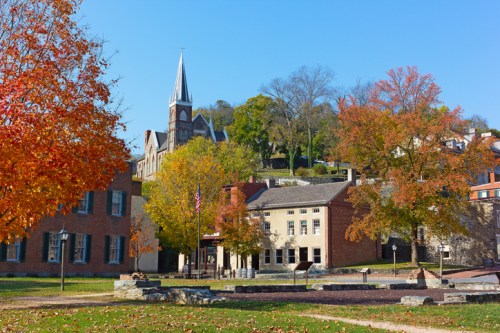 A scenic view of a town with autumn foliage, featuring a church steeple and historic buildings under a clear blue sky.