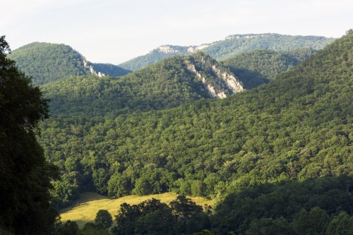 Lush green mountains with rocky cliffs and a valley, under a clear sky.