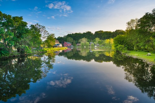 A serene river scene with lush trees and colorful reflections on the water, under a clear blue sky.