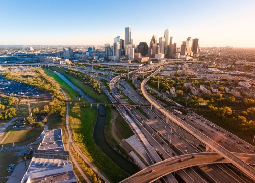 Aerial view of a city skyline with highways and green spaces, illuminated by the warm glow of sunset.