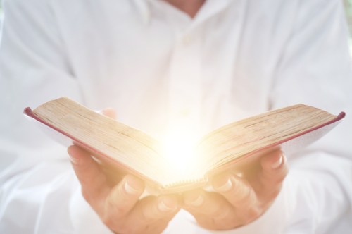 A person in a white shirt holds an open book, with a bright light emanating from its pages.