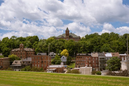 A scenic view of a small town with historic buildings and a hilltop structure under a partly cloudy sky.