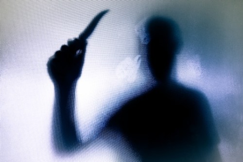 A shadowy figure holding a knife, partially obscured by a frosted surface.