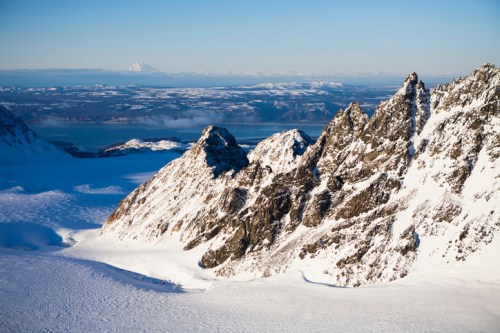 Snow-covered mountains rise above a vast glacier, with a distant peak visible under a clear blue sky.