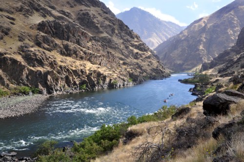 A winding river flows through a rugged canyon, surrounded by steep, rocky hills and sparse vegetation.
