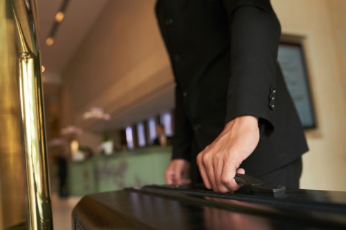 A hotel staff member in a black uniform is handling a luggage cart in a stylish lobby.