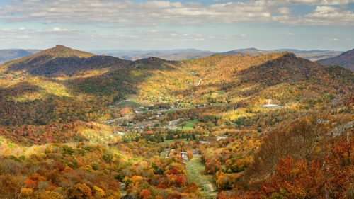 A panoramic view of a colorful autumn landscape with rolling hills and a small village nestled in the valley below.