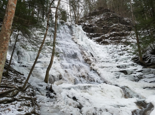 A frozen waterfall cascading down rocky terrain, surrounded by trees in a winter landscape.