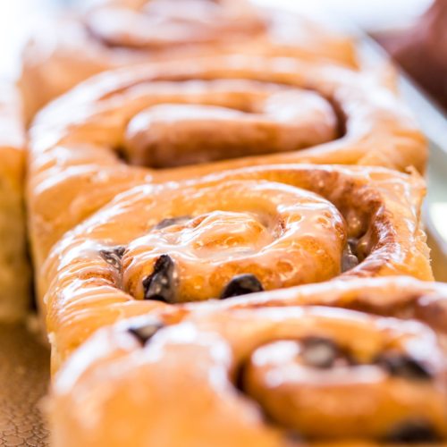 Close-up of freshly baked cinnamon rolls drizzled with icing, arranged in a row on a tray.